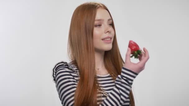 Γλυκό τζίντζερ κοπέλα είναι δάγκωμα φράουλα, απολαμβάνοντάς το, λευκό φόντο — Αρχείο Βίντεο