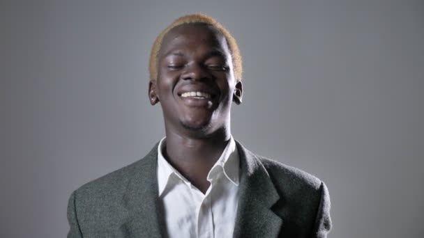 Joven hombre rubio afroamericano en traje sonriendo y mirando a la cámara, aislado sobre fondo gris — Vídeos de Stock