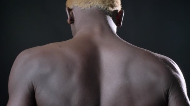 Afrikaanse gespierde jongeman draaien rond en kijken camera, permanent in een studio, geïsoleerd op zwarte achtergrond — Stockvideo