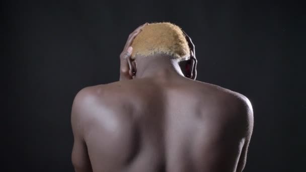Costas nuas do jovem africano cobrindo seus ouvidos, em pé sozinho, isolado no fundo preto — Vídeo de Stock