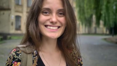 Kamera dişli gülümseyen ve üniversite Parkı ayakta uzun saçlı Genç büyüleyici kadın