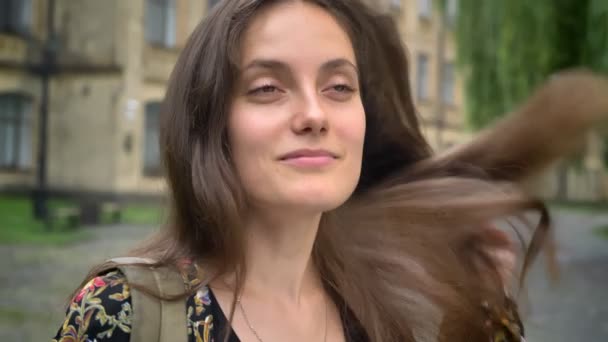 Молода красива жінка з довгим волоссям, що стоїть на вулиці, повертаючись і дивлячись на камеру, концепція студента — стокове відео