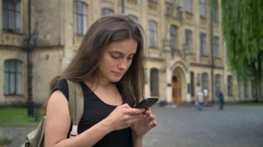 Cep telefonundan yazarak ve Parkı Üniversitesi, sırt çantası tutan kadın ayakta genç güzel beyaz öğrenci
