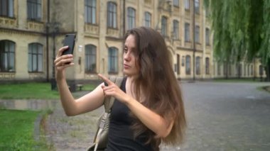 Cep telefonu üzerinden görüntülü sohbet sahip ve söz, sokakta bina university yakınındaki ayakta beyaz güzel kadın