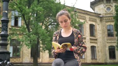 Kitap okuma ve kampüs bina, cadde bankta oturan genç Şirin üniversite öğrencisi konsantre ve belirlenen