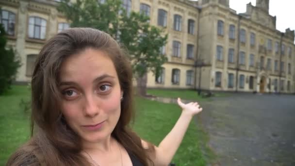 Joven mujer hermosa blogger tiroteo blog o tener chat de vídeo, de pie en el parque cerca del edificio de la universidad, sonriendo — Vídeo de stock