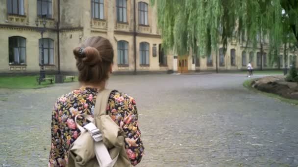 Unga glada kvinnliga högskolestudent med ryggsäck kommer till college, gå på gatan nära university, vackra och charmiga — Stockvideo