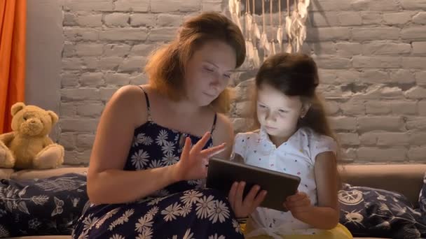 Küçük kız ve tablete yazma ve ile Aile kavramı kapalı modern adlı ana sayfa, kanepede oturan genç anne — Stok video