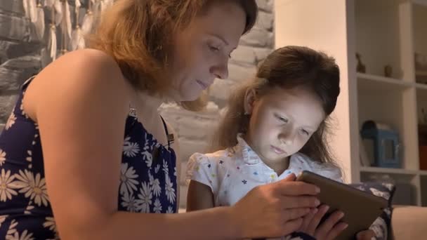 Madre con hija pequeña usando la tableta y sentada en el sofá en el hogar moderno, concepto de familia con gadget, en el interior — Vídeos de Stock