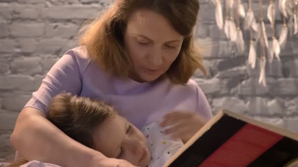 Mutter liest kleinen Tochter Buch, Kind liegt auf dem Schoß der Eltern und hört Schwanz, Familienkonzept zu Hause, drinnen — Stockvideo