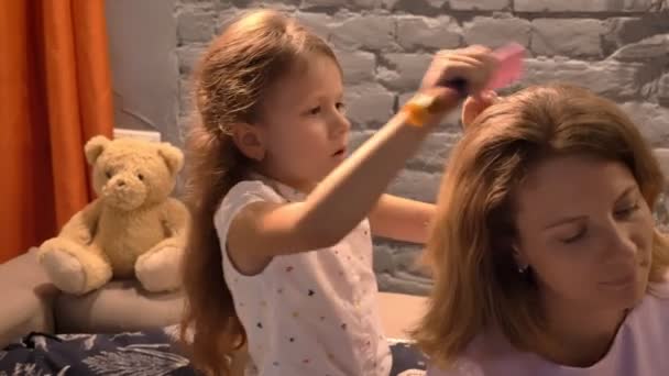 Kleines Mädchen, das seiner Mutter die Haare mit der Haarbürste bürstet, moderner Wohnzimmerhintergrund, Familienkonzept im Haus — Stockvideo