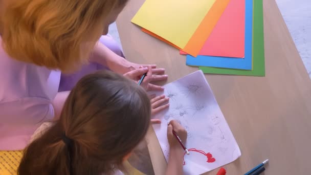 Top shot, madre enseñando a su hija a dibujar en papel, padres e hijos sentados juntos y haciendo tareas, concepto familiar — Vídeos de Stock