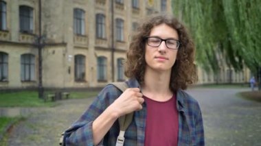 Genç yakışıklı adam gözlüklü ve sırt çantası üniversite kampüs, öğrenci kavram Parkı ile kıvırcık saçlı ayakta ile