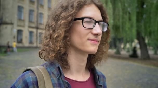 Νεαρός φοιτητής με μακριά σγουρά μαλλιά κουνώντας και ανυπομονησία, στέκεται στο δρόμο κοντά στο κολέγιο ή πανεπιστημιούπολη — Αρχείο Βίντεο