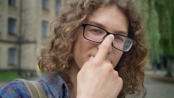 Schöner selbstbewusster Student, der seine Brille anfasst und in die Kamera lächelt, auf der Straße in der Nähe der Universität stehend, fröhlich und lustig — Stockvideo