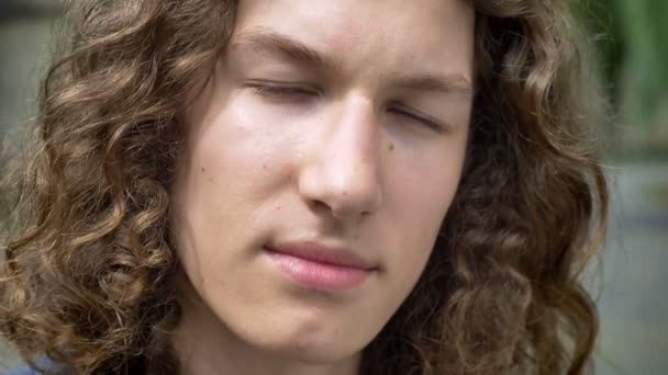 Yakın kamera, konsantrasyon ve kararlılık bakarak uzun kıvırcık saçlı Genç ciddi yakışıklı adam portresi — Stok video