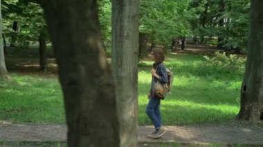 Nerdy üniversite öğrencisi Park'ta yürüyordunuz ve sabırsızlıkla, ağaç ve otların çevresinde, güneş ışığı açık havada uzun kıvırcık saçlı