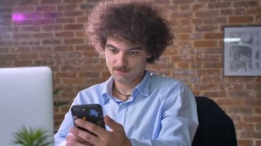 Komik inek Patron telefonda yazarak ve ekran kamera, modern ofisinde oturan içine gösterilen birim kıvırcık saçlı