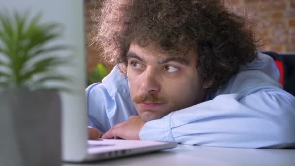 Набридливий нервовий бос з кучерявим волоссям і вусами лежить на столі і працює на ноутбуці, сучасний офісний фон — стокове відео