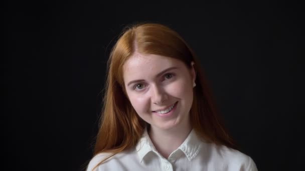 Young charming woman with ginger hair in white shirt smiling at camera, isolated on black background — Stock Video