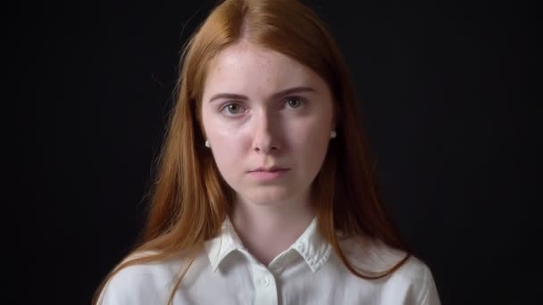 Allvarlig ung kvinna med ingefära hår tittar kameran med berörda och ockuperade uttryck, svart bakgrund — Stockvideo