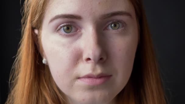 Nauwe portret van jonge ernstige mooie vrouw gezicht kijken camera met betrokken en bezette expressie, zwarte achtergrond — Stockvideo