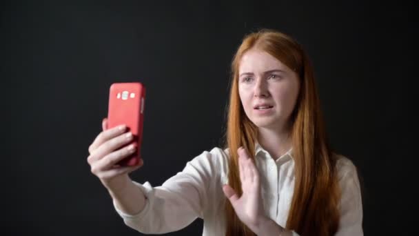 Charming teenage girl with long ginger having video chat through phone, isolated on black background smiling — Stock Video