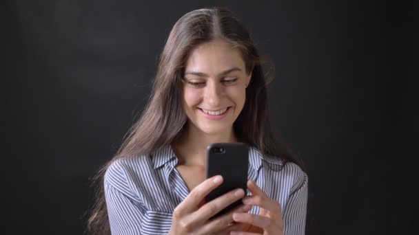 Молода красива жінка має відеочат через мобільний телефон, розмовляє і посміхається, ізольована на чорному тлі — стокове відео