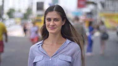 Mutlu genç güzel kadın kameraya gülümseyen ve kentsel sokakta duran uzun saçlı