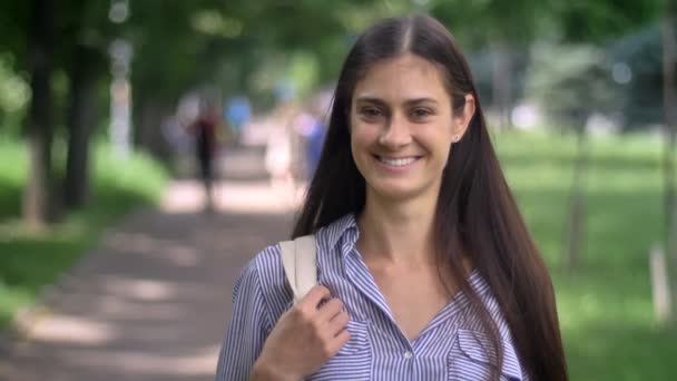 Uroczy szczęśliwy młody student kobieta stojąc w parku i uśmiechnięty, trzyma plecak — Wideo stockowe