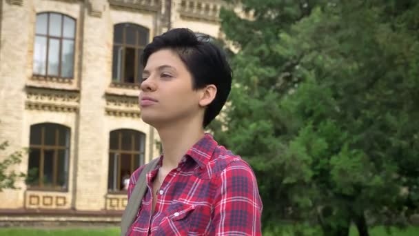 Heureux jeune étudiant avec les cheveux courts noirs souriant et debout dans le parc près de l'université — Video
