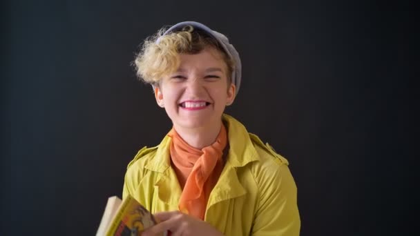 Hermosa mujer feliz en chaqueta amarilla aprendiendo el idioma francés y sonriendo a la cámara, aislado sobre fondo negro — Vídeos de Stock