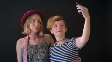İki sevimli genç sarışın kadınlar üzerinde sarılma ve selfie, ayakta alarak izole siyah arka plan.