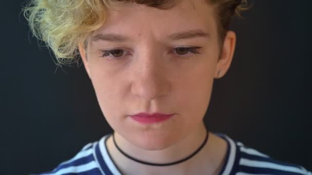 Porträtt av allvarlig ung kvinna med lockigt blont hår tittar på kameran, isolerad på svart bakgrund — Stockvideo