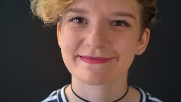 Portrait of pretty young woman with curly hair smiling and blinking into camera, isolated on dark background — Stock Video