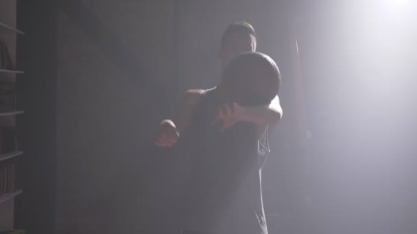 Баскетболіст, який виконує різні трюки і обертається м'яч у темному тренажерному залі з димом — стокове відео