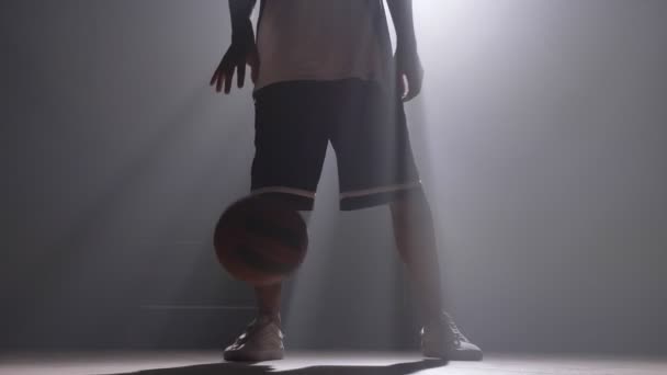 Een basketballer dribbelen de bal in mistige donkere kamer met floodlight — Stockvideo