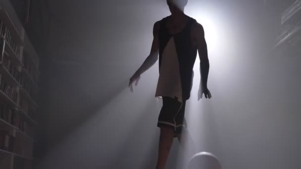 Uma silhueta de jogador de basquete jogando com bola em quarto escuro enevoado com projector — Vídeo de Stock