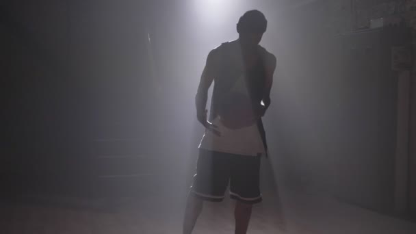 Ένας μπασκετμπολίστας που παίζει με μπάλα σε θολό τοπίο σκοτεινό δωμάτιο με προβολείς — Αρχείο Βίντεο
