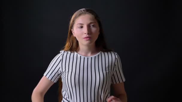Rasende ung kvinne som står med kryssede hender og ser på kamera med sinte og bekymrede uttrykk, svart bakgrunn – stockvideo