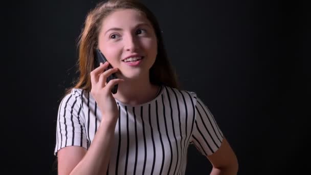 Krásná veselá zázvor mladá žena mluví o telefonu, usměvavý, stojící na černé studio pozadí