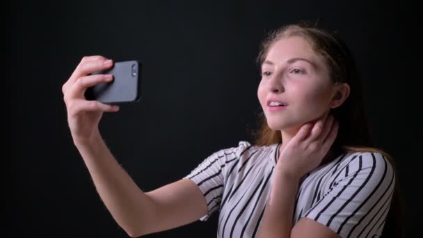 Kızıl saçlarını alarak selfie ve gülümseyerek, siyah stüdyo arka plan üzerinde izole ayakta büyüleyici mutlu kadınla — Stok video