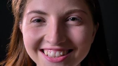 Yakın gülüyor ve siyah arka plan üzerine izole kamera, gülümseyen Genç Sevimli kadın portresi