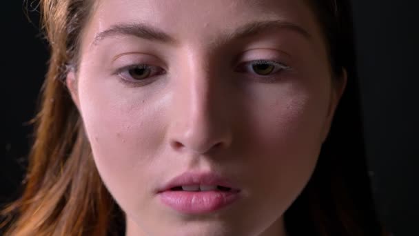 Retrato de perto de uma jovem séria olhando para a câmera, isolada no fundo do estúdio preto, preocupada e concentrada — Vídeo de Stock