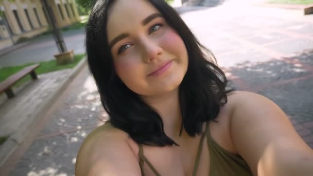 Belle jeune femme obèse prenant selfie ou tournage vidéo avec sa caméra web sur son téléphone, debout dans la rue près de l'université — Video