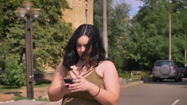 電話の通り、日当たりの良い天気の屋外、魅力的なブルネットの女性の上を歩く美しい若い肥満女性のテキスト メッセージ — ストック動画
