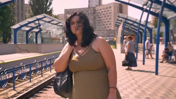 Hermosa mujer obesa joven con mochila esperando y buscando tren, de pie en la plataforma en la estación urbana — Vídeo de stock