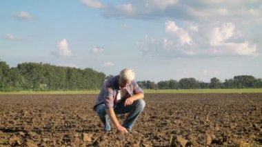 Alanında oturup ve tek elle, sıcak yaz günü sırasında ayakta toprak kapma yaşlı çiftçi