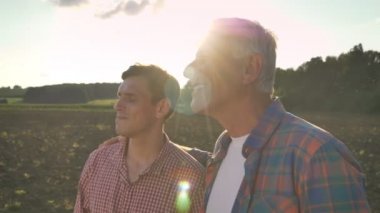 Yaşlı baba oğlu kucaklayan ve ekili alan, güzel görünümlü arka planda günbatımı, Mercek parlaması sırasında görüntülemek