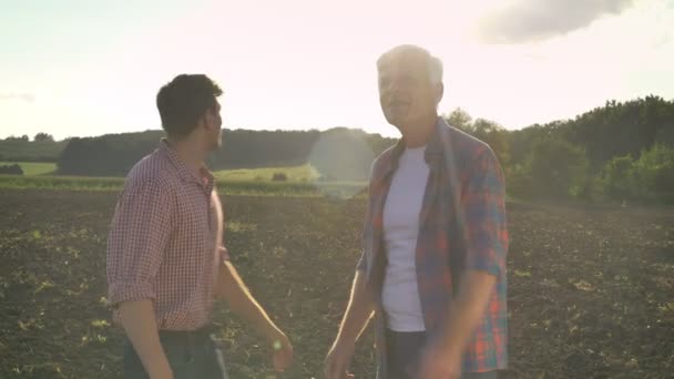 Glücklicher alter Vater zeigt seinem Sohn bestelltes Feld und lächelt, schöne Natur im Hintergrund des Sonnenuntergangs — Stockvideo